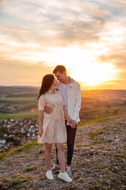 A couple in love, a guy and a girl are standing on a mountain at sunset hugging and kissing