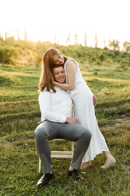 Couple in love hug and have fun at sunset on a sunny day. the guy sits on a chair and keeps his wife on his knees. family walk