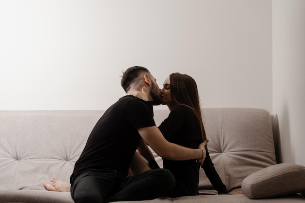 Couple in love hugging and kissing on couch at home Love story of a couple spending time in cozy room at home Relationships feelings and tenderness in the family of men and girl