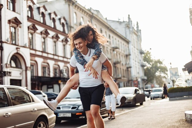 Couple in love Man carrying girl on his back in the street Smiling man with beautiful young woman ride piggyback having fun together Relationship concept