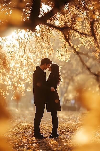 A couple in love silhouetted against the golden glow of autumn leaves stand close to each other in a park