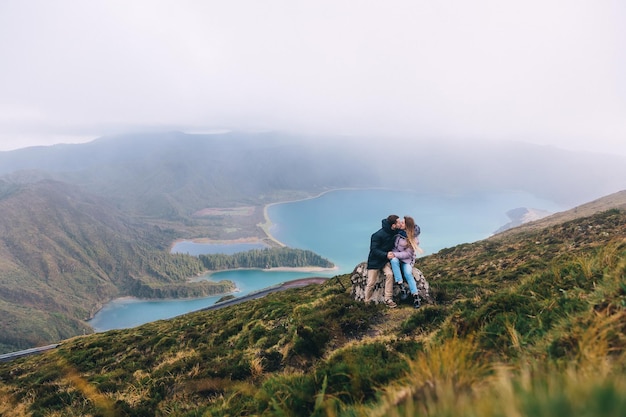 A couple in love sits on a stone kissing against the backdrop of a lake sky nature travel rest