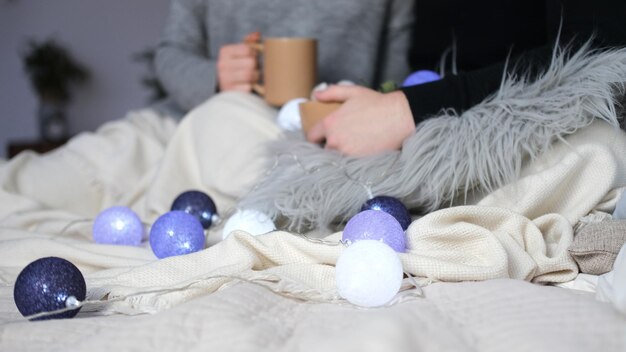 A couple in love sits wrapped in a blanket with cups in their hands In the foreground lies a garland of balloons