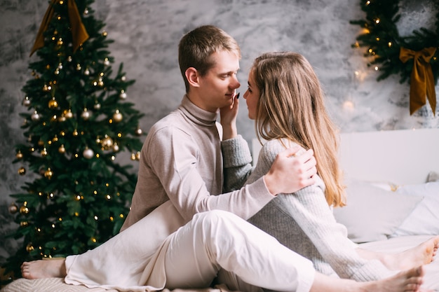 Couple in love sitting next to a Christmas tree on bed at home