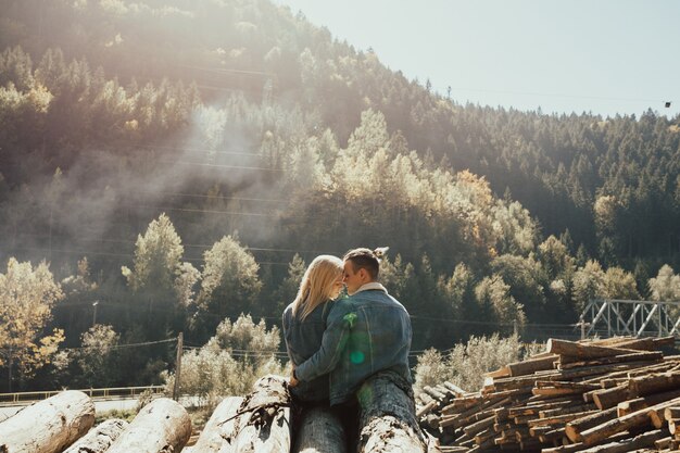 Photo a couple in love sitting on the stack of firewood in the beautiful colorful autumn forest.