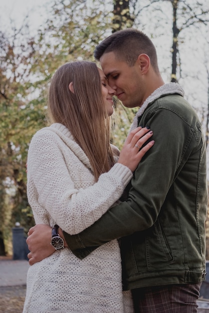 Couple in love stand on autumn fallen leaves in a park, enjoying a beautiful autumn day.