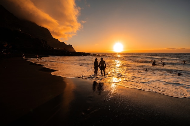 A couple in love stands in the ocean in the evening looking at the beautiful sunset on the island of Tenerife.Spain.