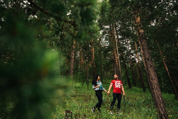 A couple in love walks through the coniferous forest. Guy and girl walking in the woods. Man and woman holding hands. Couple in green forest. The couple in love hold hands in the forest. Follow me