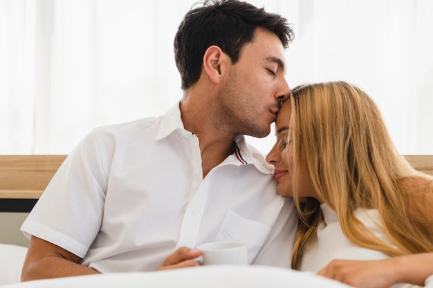 Couple lover smiling and making warm kiss on woman forehead in bedroom