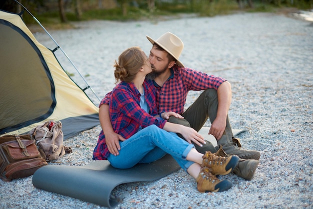 Couple of lovers sit in camping hugs and kiss spent time together in weekend