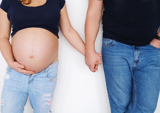 A couple a man and a pregnant woman stand near a white wall and hold hands The concept of support and love in the family