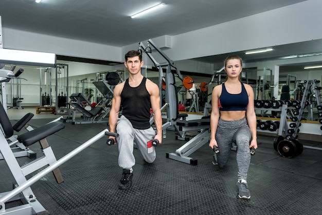 Couple of man and woman doing exercises together in gym