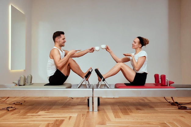 Couple man woman drinking tea coffee during palates training on the reformer people train in the gym