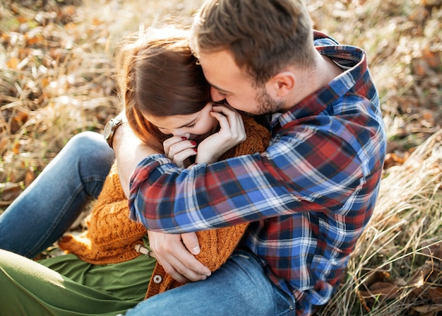 Couple of man and woman laughing, sitting in a field outdoors, man hugging woman.