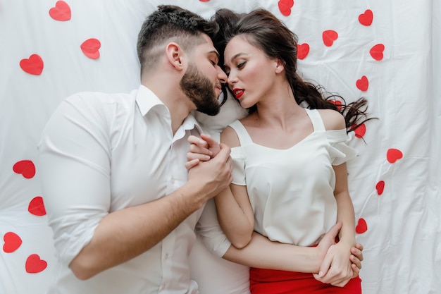 Couple man and woman in love on bed with red heart shapes at home