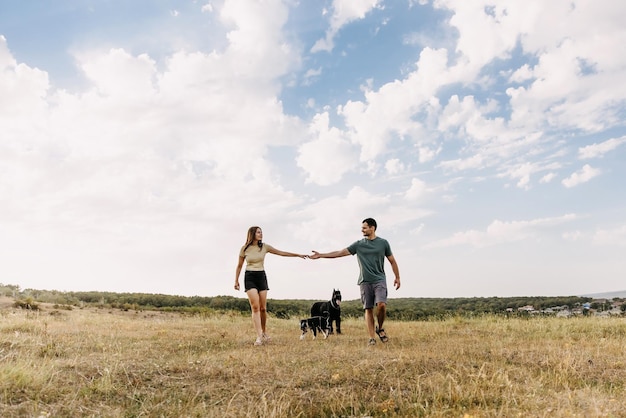 Couple of man and woman walking in an open field with two dogs