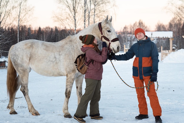 Photo couple man and woman walking with white horse in winter day in countryside