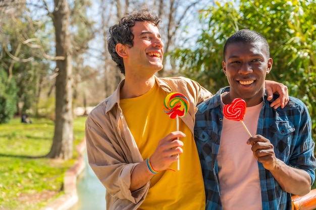 Couple of multi ethnic men eating a lollipop lgbt concept having fun and smiling in a park