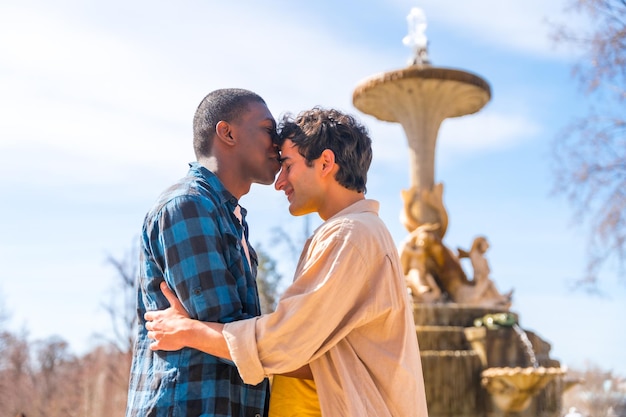 Couple of multiethnic men in a city fountain lgbt concept in a romantic pose kissing each other on the forehead