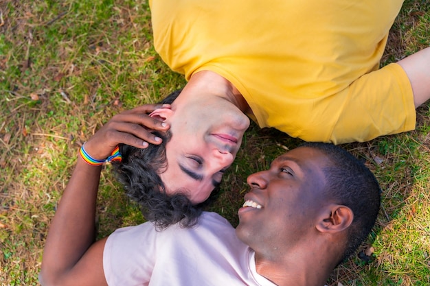 Couple of multiethnic men in a park lgbt concept lying on the grass in a romantic pose