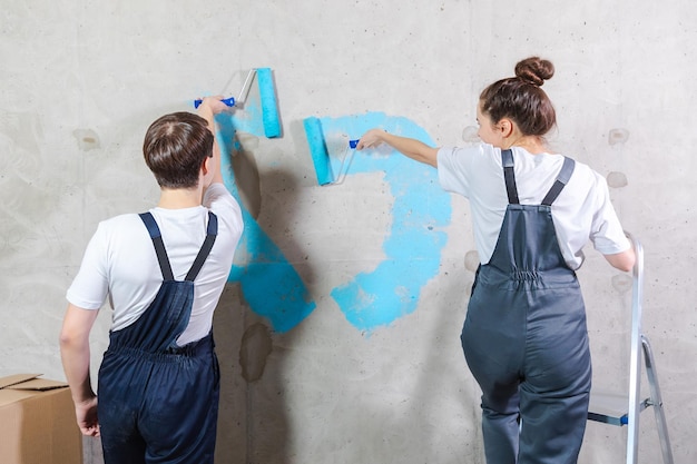 Couple in new home during repair works painting wall together Happy family holding paint roller painting wall with blue color paint in new house Home renovation DIY renew home concept