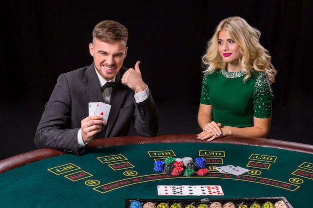 Couple playing poker at the green table. The blonde girl and a guy in a suit. happy win, two aces