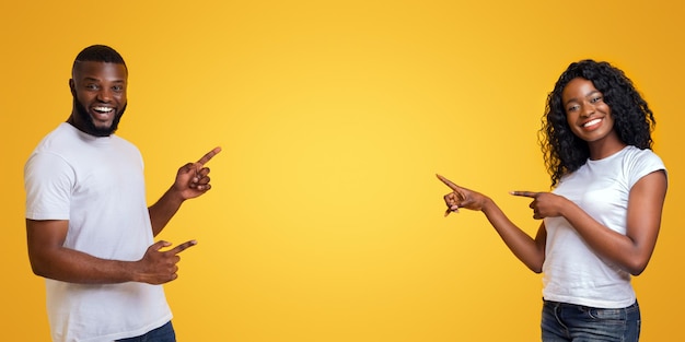 Couple Pointing Towards Empty Space on Yellow Background