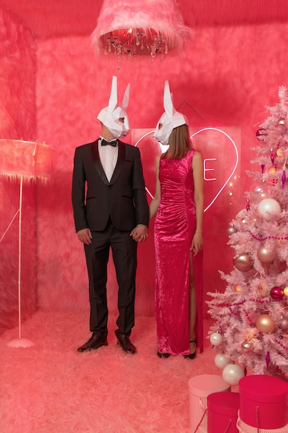 The couple in poligonal rabbit masks closeup on the pink background are celebrating New 2023 year. C