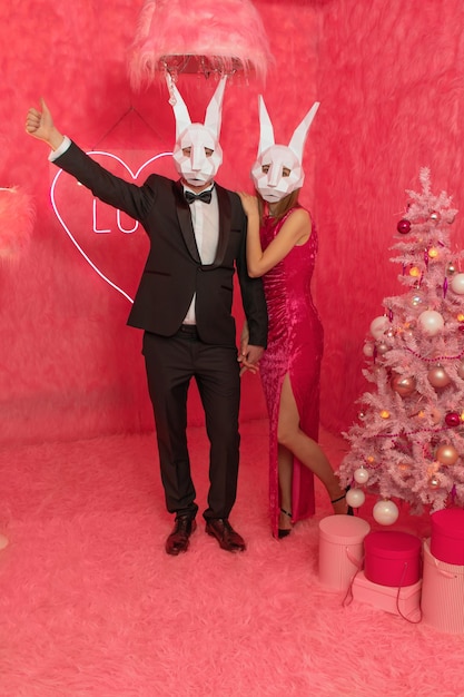 The couple in poligonal rabbit masks closeup on the pink background are celebrating New 2023 year. C