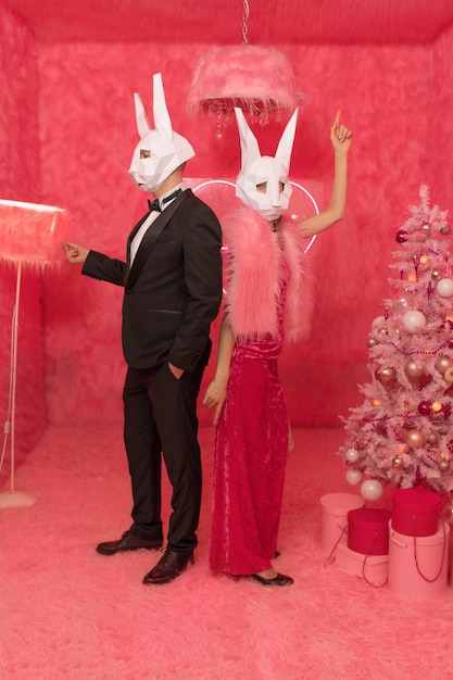 The couple in poligonal rabbit masks closeup on the pink background are celebrating New 2023 year. C