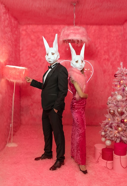 The couple in poligonal rabbit masks closeup on the pink background are celebrating New 2023 year. C