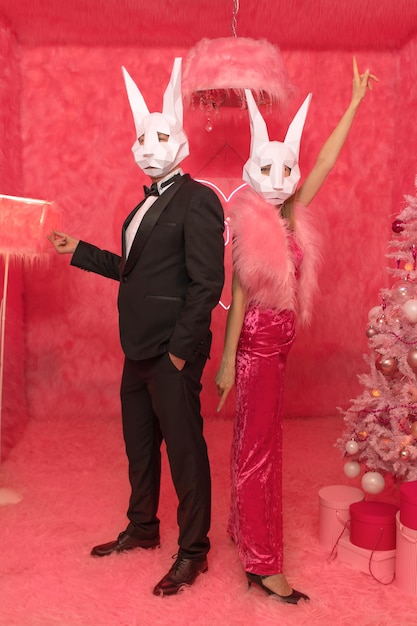 The couple in poligonal rabbit masks closeup on the pink background are celebrating New 2023 year. C