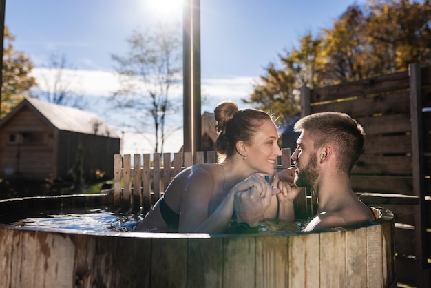 Photo couple relaxing in a private outdoor woodfired hot tub enjoying glamping amenity and spa facility