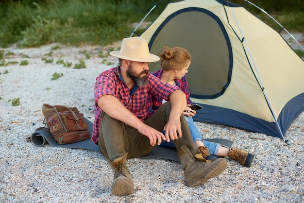 Couple resting in park White friends sitting near tent during camping together on fall day