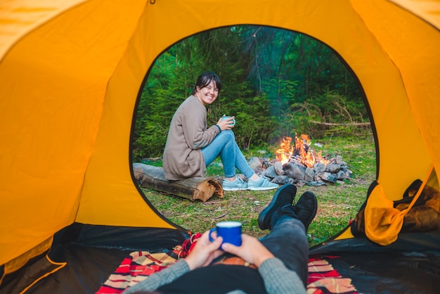 Couple resting in tent with view on fire woman drinking hot tea