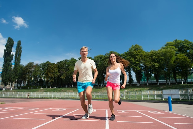 Couple running on arena track Sport and healthy fitness Runner on competition and future success Man and woman sunny outdoor on blue sky Coach and trainer at workout