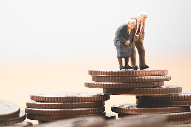 Couple Senior Pensioners miniature figure standing on the top coins stacking for wealth financial planning money saving and life insurance of retirement concept