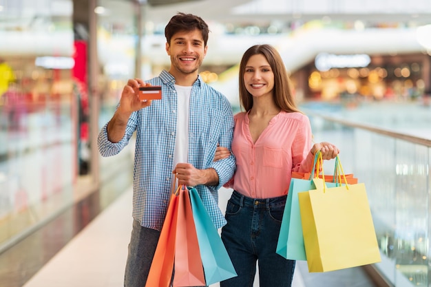 Couple shopping showing credit card holding shopper bags in hypermarket