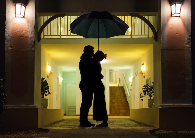 Photo couple in silhouette kissing under umbrella