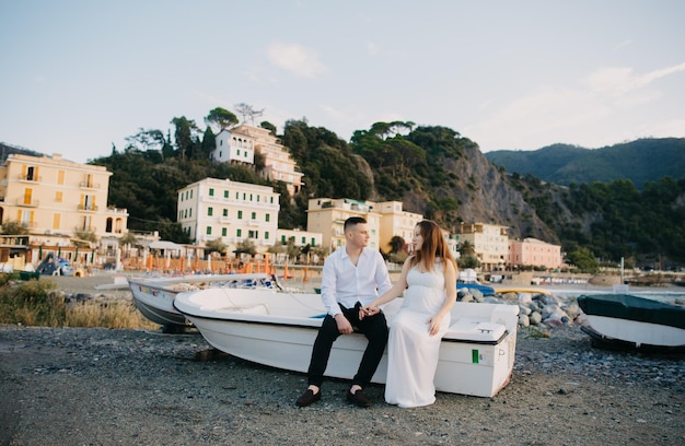 A couple sits on a boat on the beach in front of a mountain