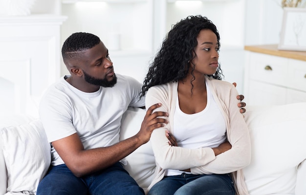 A couple sits on a white couch in a living room the man with his hand on the womans arm both looking