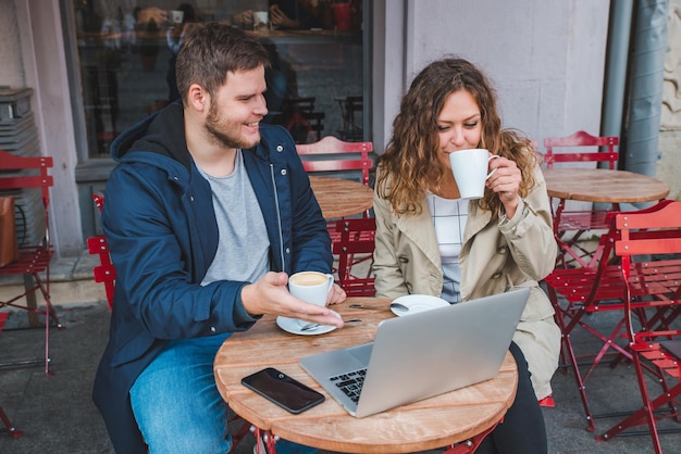 Couple sitting in cafe with laptop drinking warm up latte