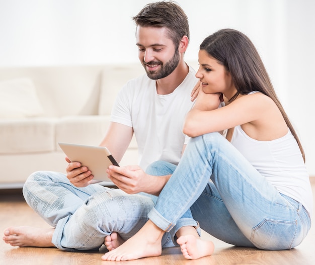 Couple sitting on floor at home and using digital tablet.