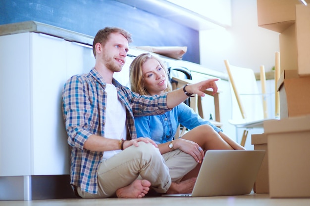 A couple sitting on the floor with a laptop and a box of things on the floor