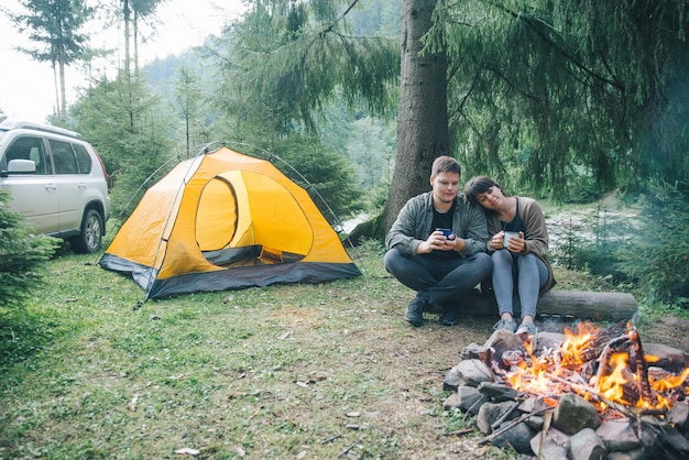 Couple sitting near fire and drink hot tea hiking concept