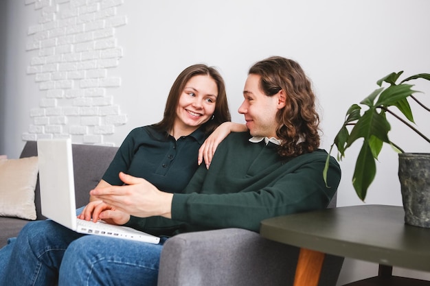 Couple sitting on the sofa with notebook and phone Man and woman communicating on the laptop phone