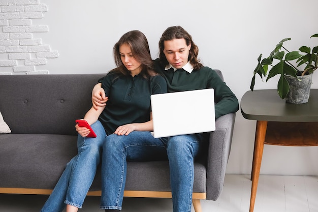 Couple sitting on the sofa with notebook and phone Man and woman communicating on the laptop phone