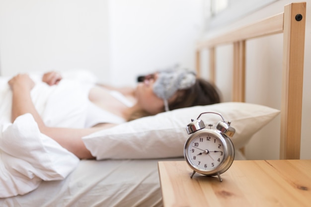 Couple sleeping on bed with alarm clock over wooden desk