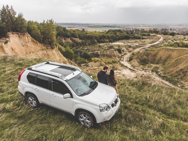 Couple standing near suv car at the cliff with beautiful view from the top