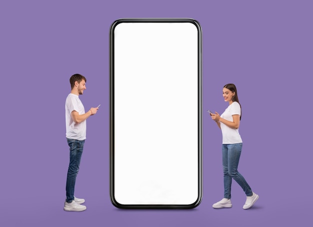 Couple standing near white empty smartphone screen and using phones